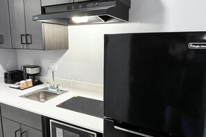 A kitchen with a black refrigerator, stainless steel sink, and a coffee maker.