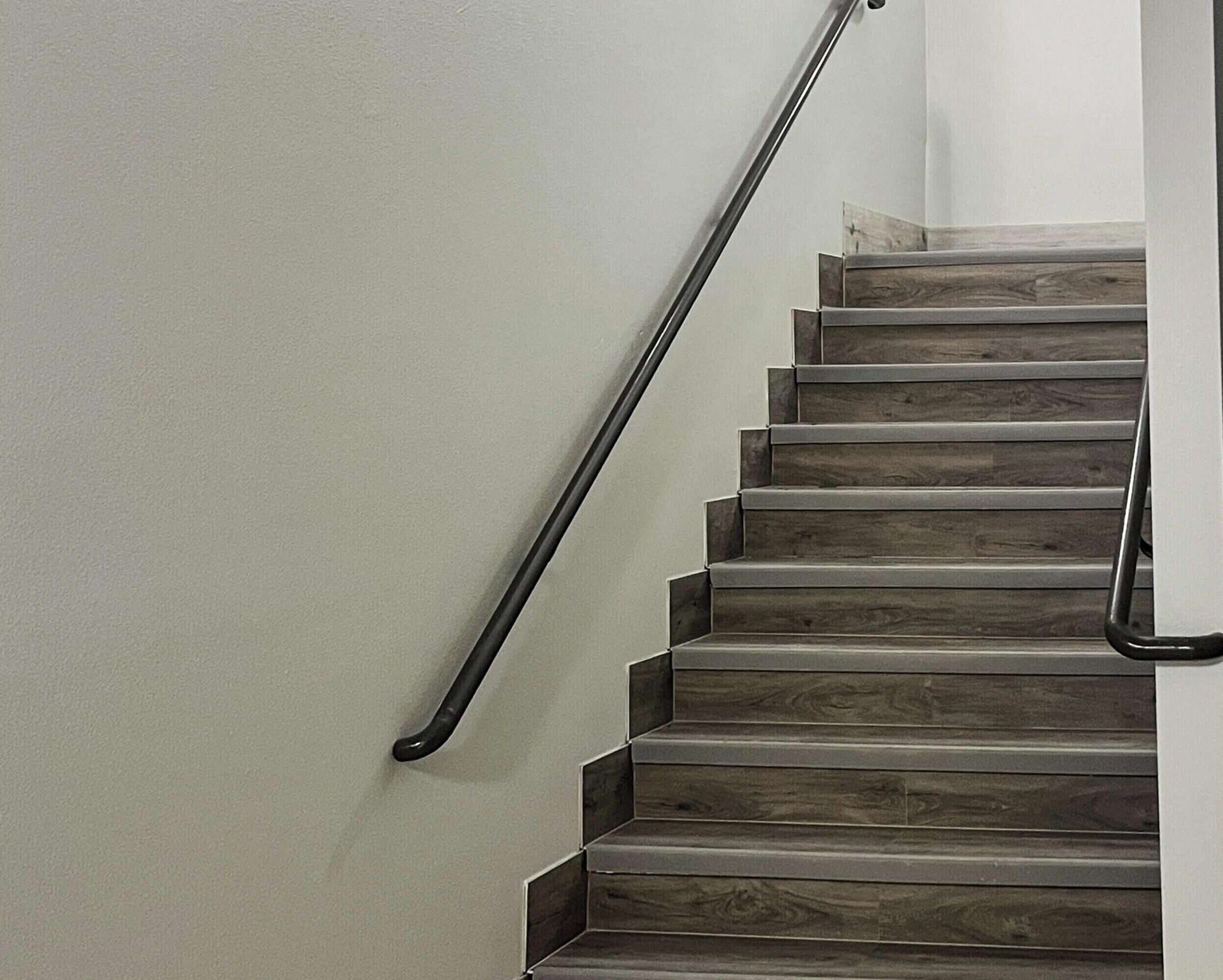 Un escalier en bois avec une rampe noire, menant à un palier.