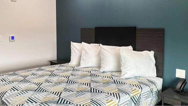 Un lit avec une couvre-lit à motifs, une tête de lit sombre et une table de chevet sur laquelle se trouve un téléphone.