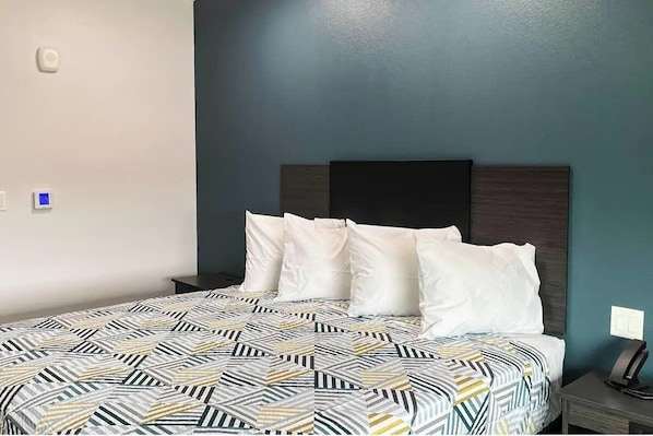 A bed with a patterned bedspread, a dark headboard, and a bedside table with a phone. - Budget-Friendly Room Near Shopping & Dining Spots | Free Parking, Pets Allowed (Houston)