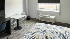 Une pièce comprenant un lit, un bureau, une chaise, une lampe sur pied, une fenêtre donnant sur un paysage agréable et un radiateur.