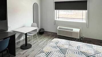 Una habitación con cama, escritorio, silla, lámpara de pie, ventana con vistas y radiador.