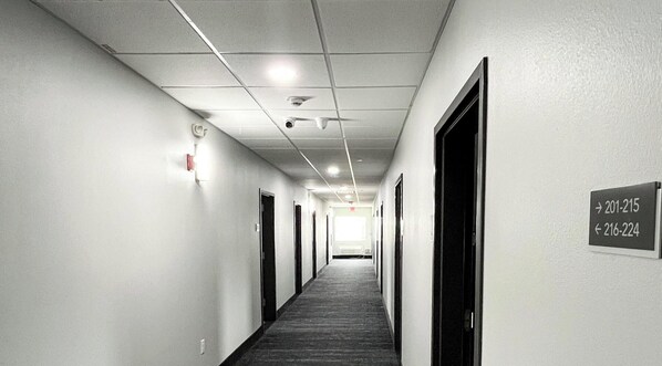 A long, narrow hallway with doors on both sides, a carpeted floor, and a ceiling with recessed lighting and smoke detectors.