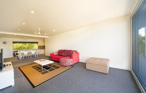 A modern living room with a red sofa, a beige ottoman, and a dining area with white chairs.
