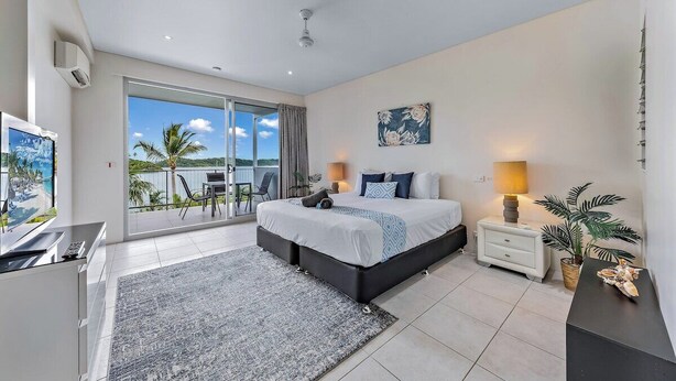 A modern bedroom with a large bed, a TV, a balcony with a view, and a dining area. - Baybliss Escape #4 - Adults Only (Shute Harbour)