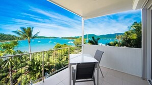 A balcony with a table and chairs, overlooking a coastal view with boats and greenery. - Baybliss Escape #4 - Adults Only (Shute Harbour)