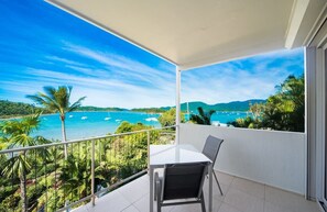 A balcony with a table and chairs, overlooking a coastal view with boats and greenery. - Baybliss Escape #4 - Adults Only (Shute Harbour)