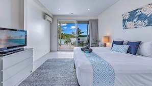 A hotel room with a bed, a television, a sliding glass door to a balcony, and a painting on the wall. - Baybliss Escape #4 - Adults Only (Shute Harbour)
