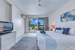 A hotel room with a bed, a television, a sliding glass door to a balcony, and a painting on the wall. - Baybliss Escape #4 - Adults Only (Shute Harbour)