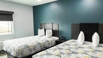 Habitación de hotel con dos camas, una ventana y una pared de acento en color verde azulado oscuro.