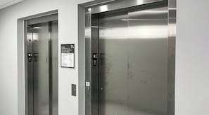 Deux portes d’ascenseur, l’une affichant les consignes de sécurité en cas d’urgence et l’autre indiquant les étages.