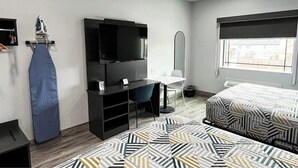 Ein Hotelzimmer mit Bett, Schreibtisch mit Stuhl, Fernseher, Bügelbrett und Fenster.