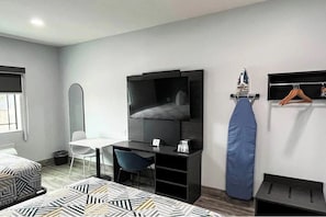 Ein modernes Hotelzimmer mit einem Bett, einem Schreibtisch mit Stuhl, einem Fernseher und einer Kleiderstange.