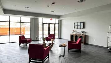 Una habitación amplia con ventanas grandes, un sillón rojo, una mesita redonda y un aparador con objetos decorativos.