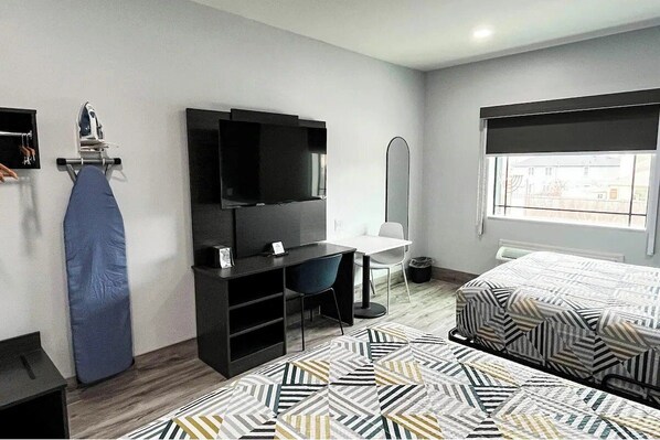 A hotel room with a bed, a desk with a chair, a TV, an ironing board, and a window. - 3 Budget-Friendly Rooms | 6.4 Miles Away from Airport | Pets Allowed (Houston)