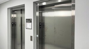 Deux portes d’ascenseur, l’une affichant les consignes de sécurité en cas d’urgence et l’autre indiquant les étages.