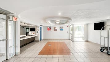 A spacious lobby with a tiled floor, an exit sign, a reception desk, and a cart.