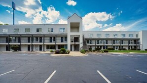 A multi-story motel with a central entrance, parking lot, and a clear sky. - Augusta King Room w/ Kitchenette Near Riverwalk Entertainment (Augusta)