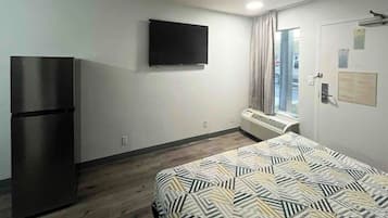 A hotel room with a bed, a flat-screen TV, a refrigerator, and a window with curtains.