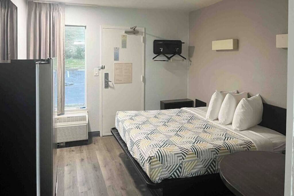 A hotel room with a bed, a desk, a chair, a window, and a door.