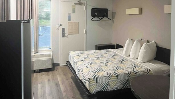 A hotel room with a bed, a desk, a chair, a window, and a door. - Augusta King Room w/ Kitchenette Near Riverwalk Entertainment (Augusta)