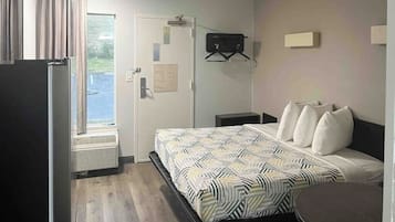 A hotel room with a bed, a desk, a chair, a window, and a door.