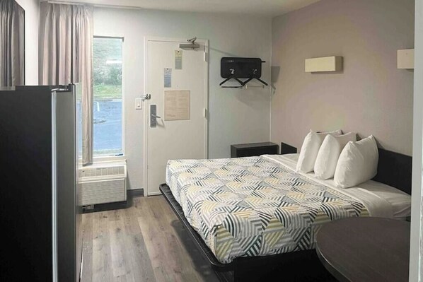 A hotel room with a bed, a desk, a chair, a window, and a door. - Augusta King Room w/ Kitchenette Near Riverwalk Entertainment (Augusta)