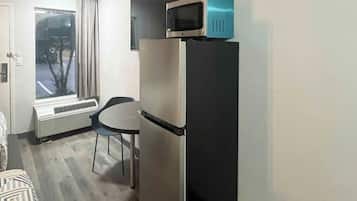 A compact room with a refrigerator, a microwave on top, a small table, and a chair.