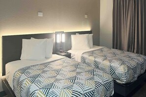 A hotel room with two beds, each with a patterned bedspread, a nightstand with a lamp, and a headboard. - Extended Stay w/ Kitchen Near Augusta Mall and Downtown Attractions (Augusta)