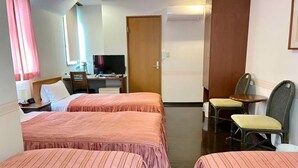 Una habitación de hotel con dos camas, un escritorio con computadora, televisión y una zona de estar con sillas.