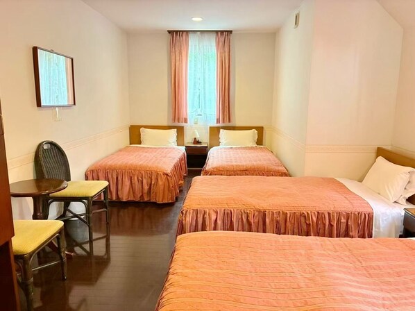 A hotel room with two single beds, a small table with a chair, a nightstand, and a window with curtains. - Vrbo Property (伊東市)