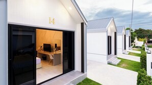 Un hotel moderno con un cartel con el número 14, una habitación visible con cama y escritorio, y un césped bien cuidado.