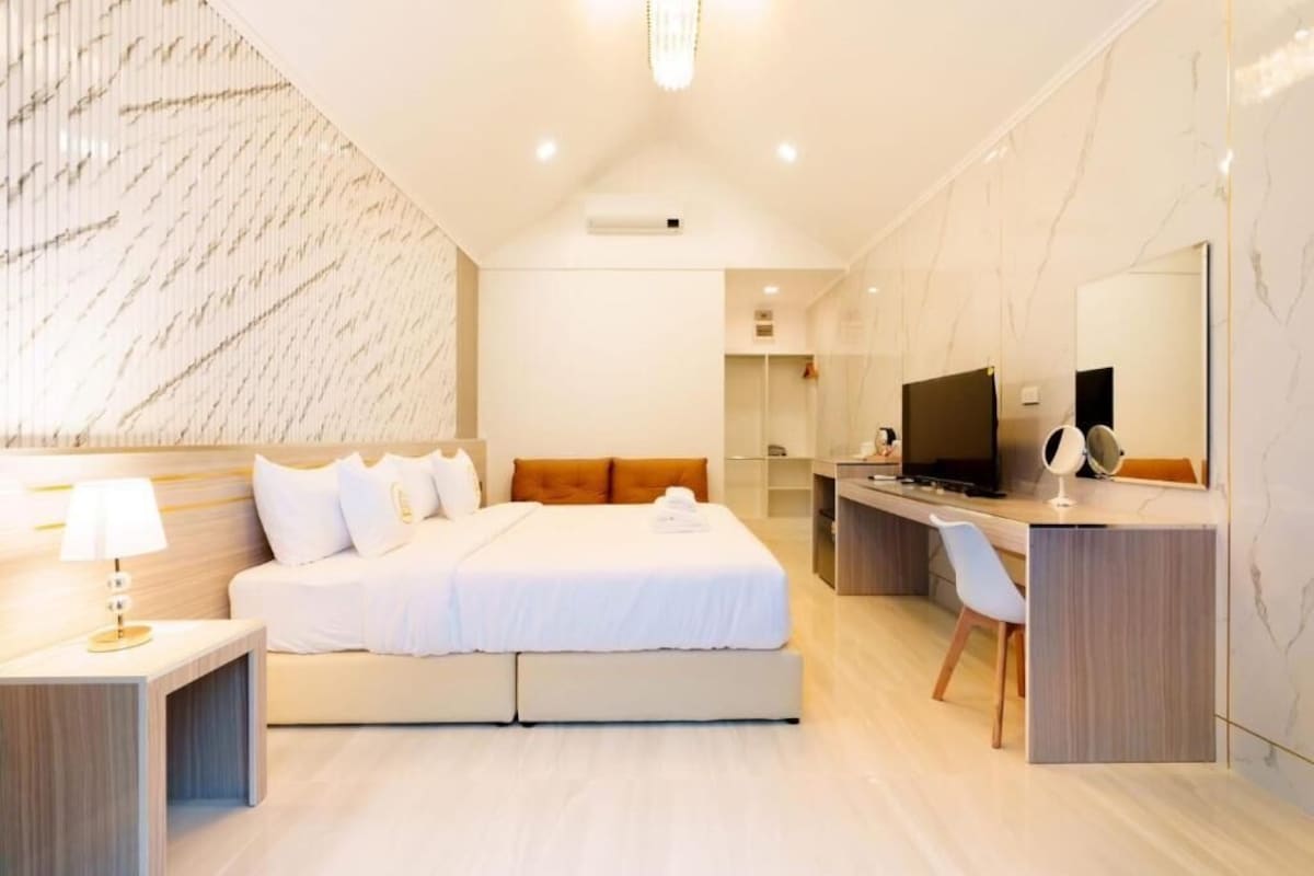 A modern hotel room with a bed, bedside table, TV, and a desk with a chair.