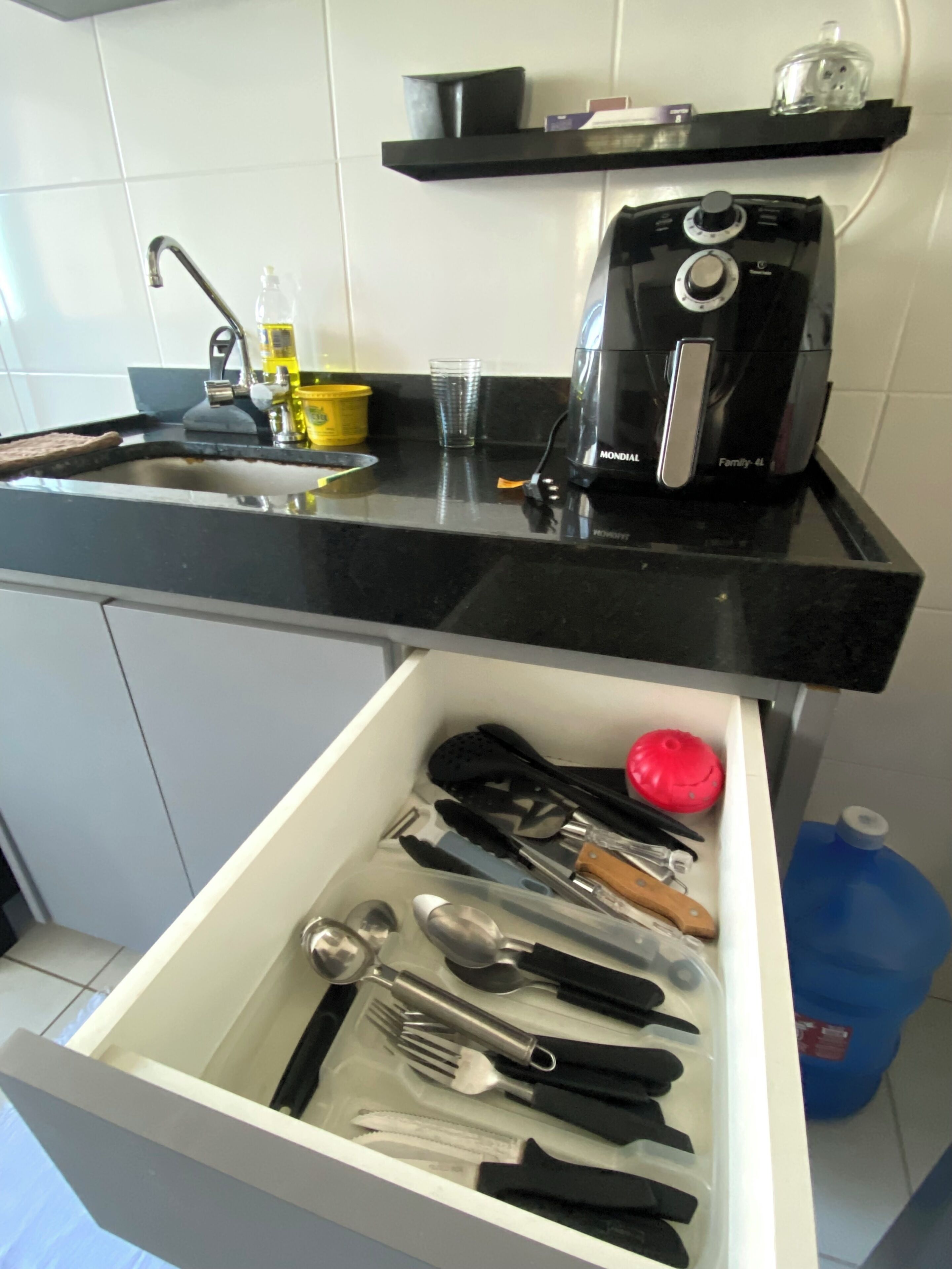 Cozinha com bancada preta, cafeteira e gaveta com utensílios.