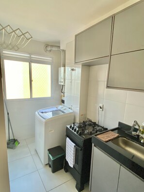 Cocina compacta con estufa a gas, un lavamanos y un ventanal que proporciona luz natural.