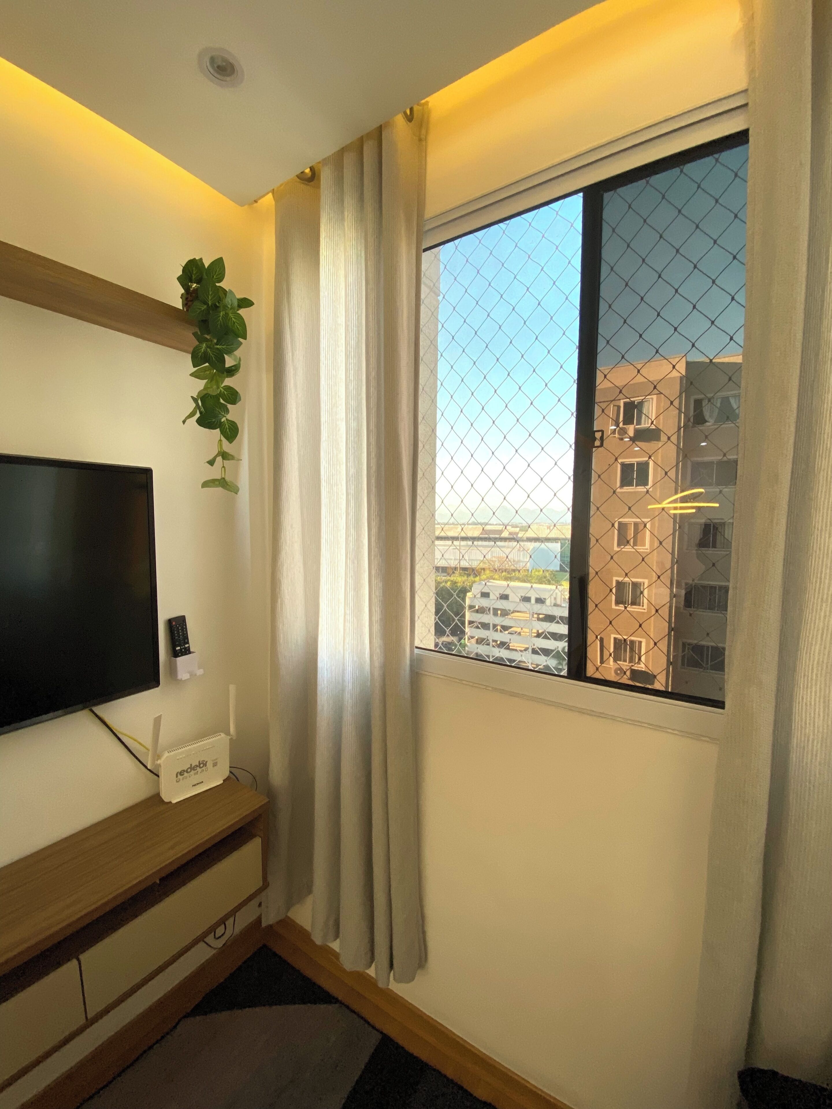 A room with a TV, a redbud router, a plant, and a window with a view of buildings.