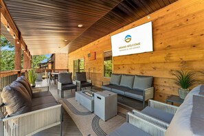 A covered outdoor seating area with modern furniture, a fire pit, and a sign welcoming guests to Grand Welcome. - Creekside Cabin Cozy Stay (Hollister)