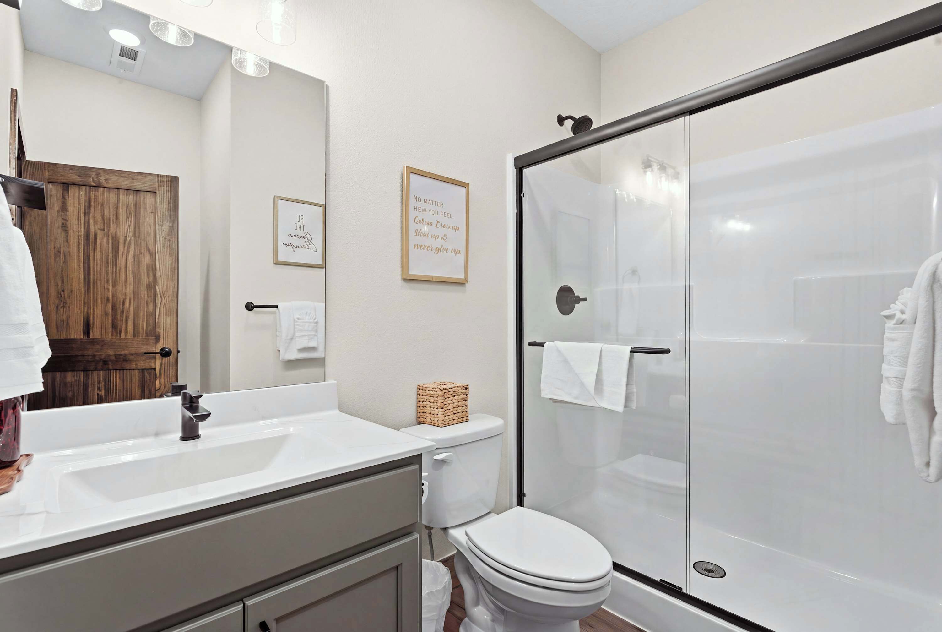 A modern bathroom with a glass shower enclosure, a white sink, and a wooden door.