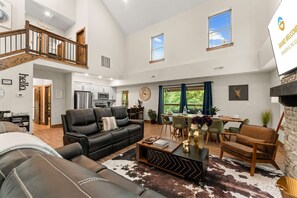 A spacious living area with a high ceiling, a staircase, a dining area with a table and chairs, and a kitchen with modern appliances. - Creekside Cabin Cozy Stay (Hollister)