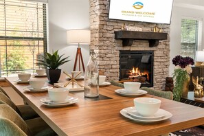 A dining area with a long wooden table set for a meal, a stone fireplace, and a sign reading 'Grand Welcome Branson & The Ozarks'. - Creekside Cabin Cozy Stay (Hollister)