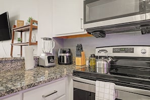 A kitchen with a granite countertop, a built-in oven, a microwave, a coffee maker, and a kettle. - New Cozy 3BR Apt - Perfect for Families & Groups (Indianapolis)