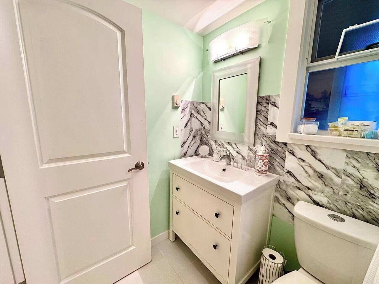 A bathroom with a white vanity, a marble backsplash, and a toilet.
