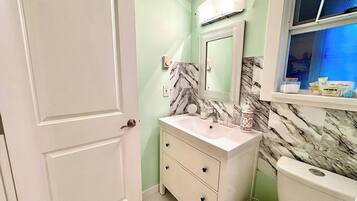 A bathroom with a white vanity, a marble backsplash, and a toilet.