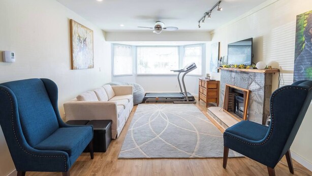 A living room with a sofa, two armchairs, a treadmill, a fireplace, and a TV. - Langley Suite Chef Kitchen (Langley Township)