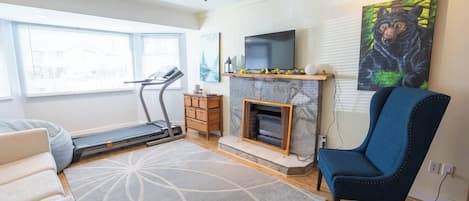 Ein Wohnzimmer mit Laufband, Kamin, blauem Sessel und einem Bärenbild an der Wand.