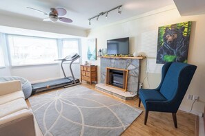 Una sala de estar con una caminadora, una chimenea, un sillón azul y un cuadro de un oso en la pared.