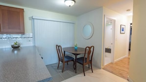 A compact kitchen with a dining area, a small table with chairs, a bowl with plants on the counter, and a white door leading to another room. - Langley Suite Chef Kitchen (Langley Township)