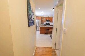 A hallway leading to a kitchen with wooden cabinets, a stainless steel refrigerator, and a microwave.