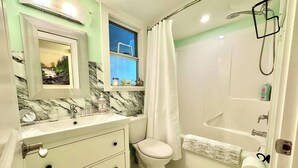 A bathroom with a toilet, sink, and shower area. - Langley Suite Chef Kitchen (Langley Township)