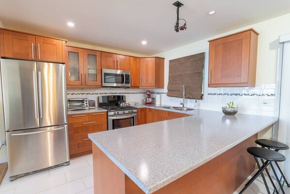 A modern kitchen with stainless steel appliances, wooden cabinets, a granite countertop, and a bar stool.